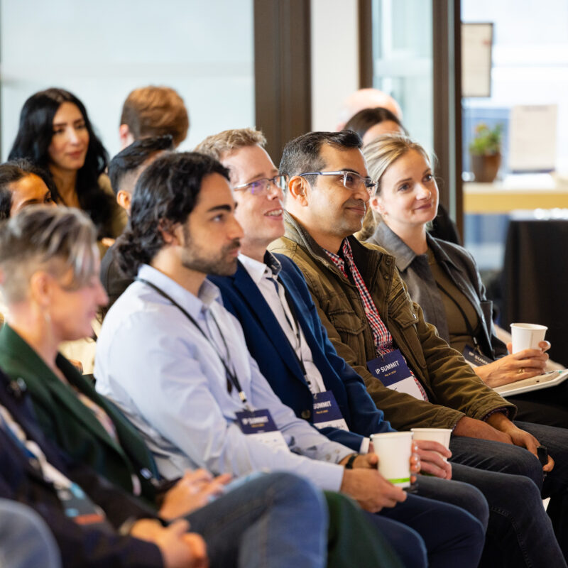 Attendees seated at the NVBC IP Summit, listening attentively to a panel of speakers at the front of the room.
