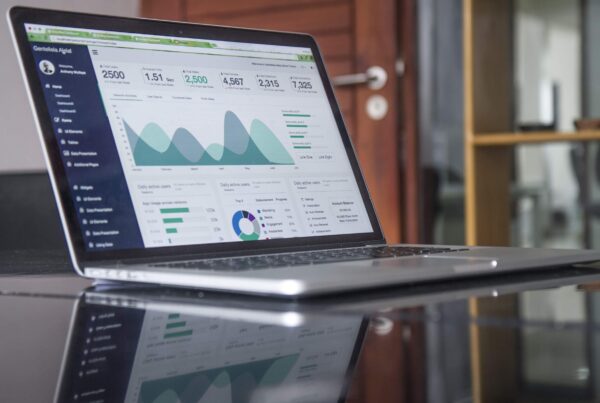 Computer sitting on glass table with different figures of graphs and charts.