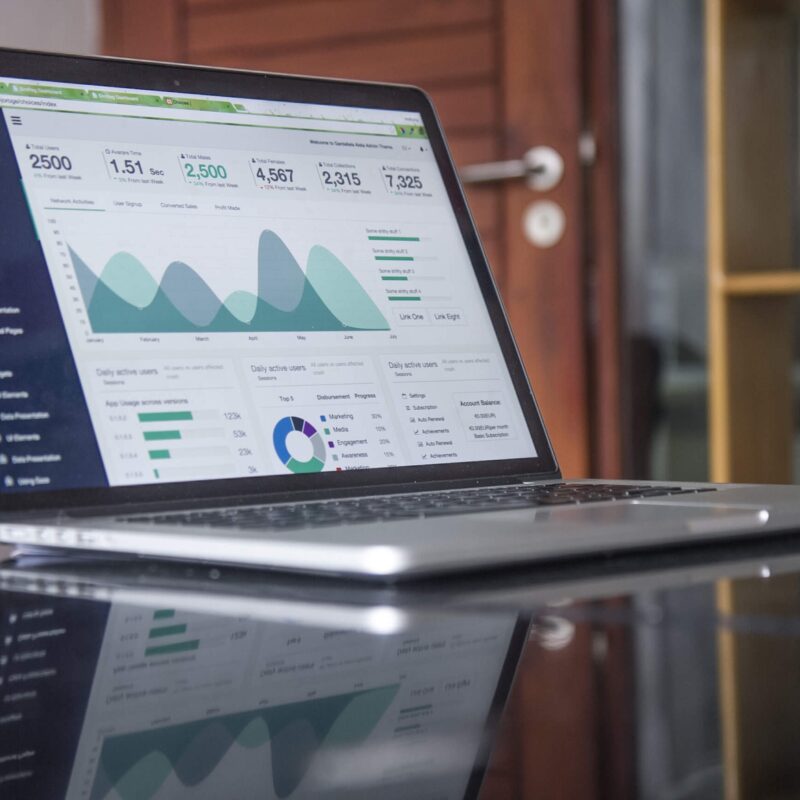Computer sitting on glass table with different figures of graphs and charts.