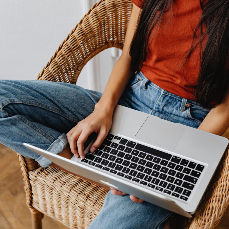 Woman sitting in a chair, typing on a laptop.
