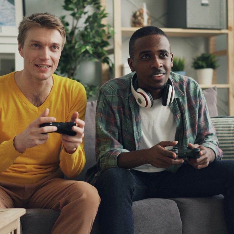 Two people sitting on a couch, smiling and holding game controllers while playing video games together.